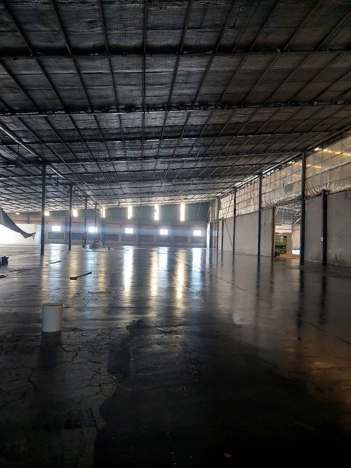 Pelapisan tahap awal epoxy gelap di area pergudangan dengan pantulan lampu langit-langit pada lapisan basah.
