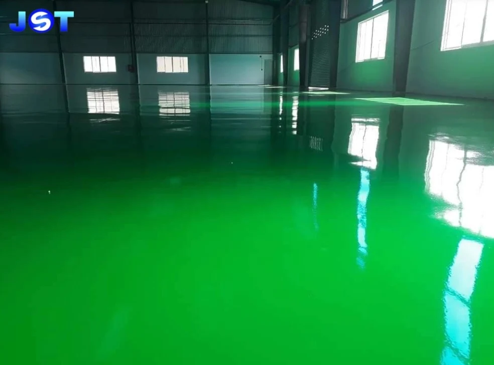 Lantai epoxy abu-abu dengan marka kuning jalur pejalan kaki dan area aman di lingkungan pabrik atau gudang.